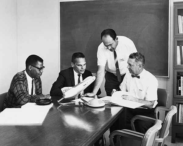 Autour de la maquette du M2F3 et du X24, debout pench&eacute; sur  le bureau Dale Reed, concepteur du projet. A sa droite,  le &laquo; cerveau &raquo; &agrave; faci&egrave;s d’extraterrestre, Ken Illif, le jeune math&eacute;maticien hyper dou&eacute;. 