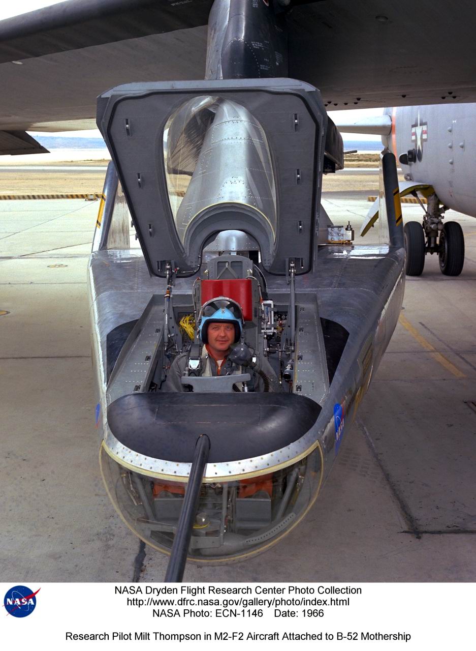 Milt Thompson, toujours aussi enthousiaste &agrave; grimper dans une des baignoires volantes (ici un M2F2), accroch&eacute; au m&acirc;t d’aile d’un B52. Noter l’excellente visibilit&eacute; vers l’avant, et la forme ramass&eacute;e du v&eacute;hicule.